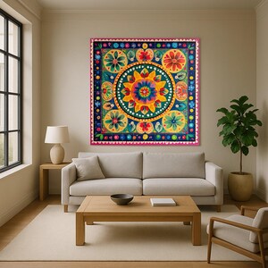 May include: A large, square, colorful wall art piece with a floral design. The artwork features a central circular pattern with yellow, orange, and blue flowers. The border is dark blue with pink and green accents. The piece is displayed in a living room setting.
