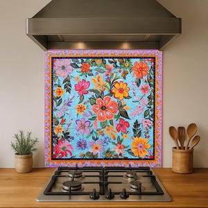 Op de afbeelding: Een bloemrijke keukenachterwand met een levendige reeks kleurrijke bloemen tegen een lichtblauwe achtergrond. Het ontwerp omvat oranje, roze en gele bloemen, omlijst door een decoratieve rand. De achterwand is geïnstalleerd boven een gaskookplaat.