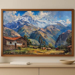 Op de afbeelding: Een ingelijst landschapsschilderij toont een bergketen met besneeuwde toppen onder een blauwe lucht. Een klein huis met een rood pannendak en grazende dieren op de voorgrond. Het kunstwerk wordt op een lichtgekleurde muur getoond.