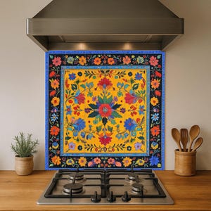 May include: A decorative floral kitchen splashback with a yellow central panel and a border of blue, black, and orange flowers. The splashback is mounted above a gas hob. The design features an intricate, ornate pattern.