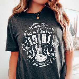 May include: Gray t-shirt with a white graphic of a guitar and the text "Legendary bad to the bone 1981".