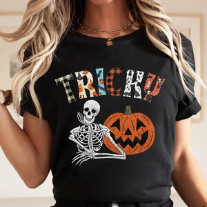 May include: Black t-shirt with a patchwork "Trick or Treat" design featuring a skeleton and a jack-o'-lantern.