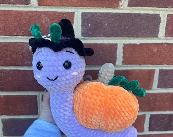 May include: A crocheted purple snail wearing a black witch hat with green accents and carrying an orange crocheted pumpkin.