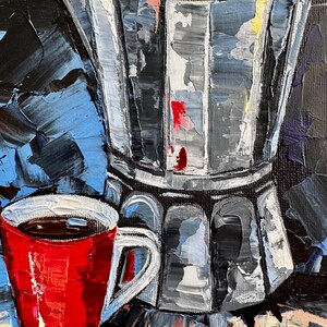 May include: A red coffee mug with a black coffee inside, sitting next to a silver and black stovetop espresso maker on a blue and yellow surface.