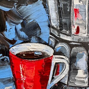 May include: A red coffee mug with a white rim and handle, filled with dark coffee. The mug is sitting on a table with a blue and gray background.