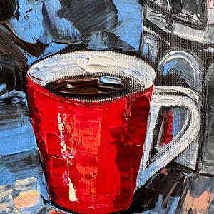 May include: A red coffee mug with a white rim and handle, filled with dark coffee. The mug is sitting on a textured surface with blue and black paint strokes.