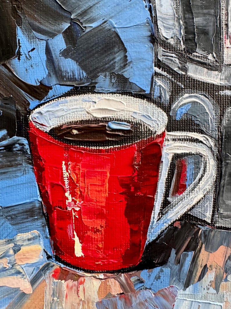 May include: A red coffee mug with a white rim and handle, filled with dark coffee. The mug is sitting on a textured surface with blue and black paint strokes.