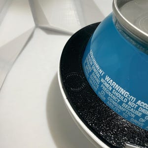 May include: A close-up shot of a blue beverage can with a silver top, resting on a black and white textured surface. The can has white text that reads, "GOVERNMENT WARNING: (1) ACCORDING TO THE SURGEON GENERAL, WOMEN SHOULD NOT DRINK..."