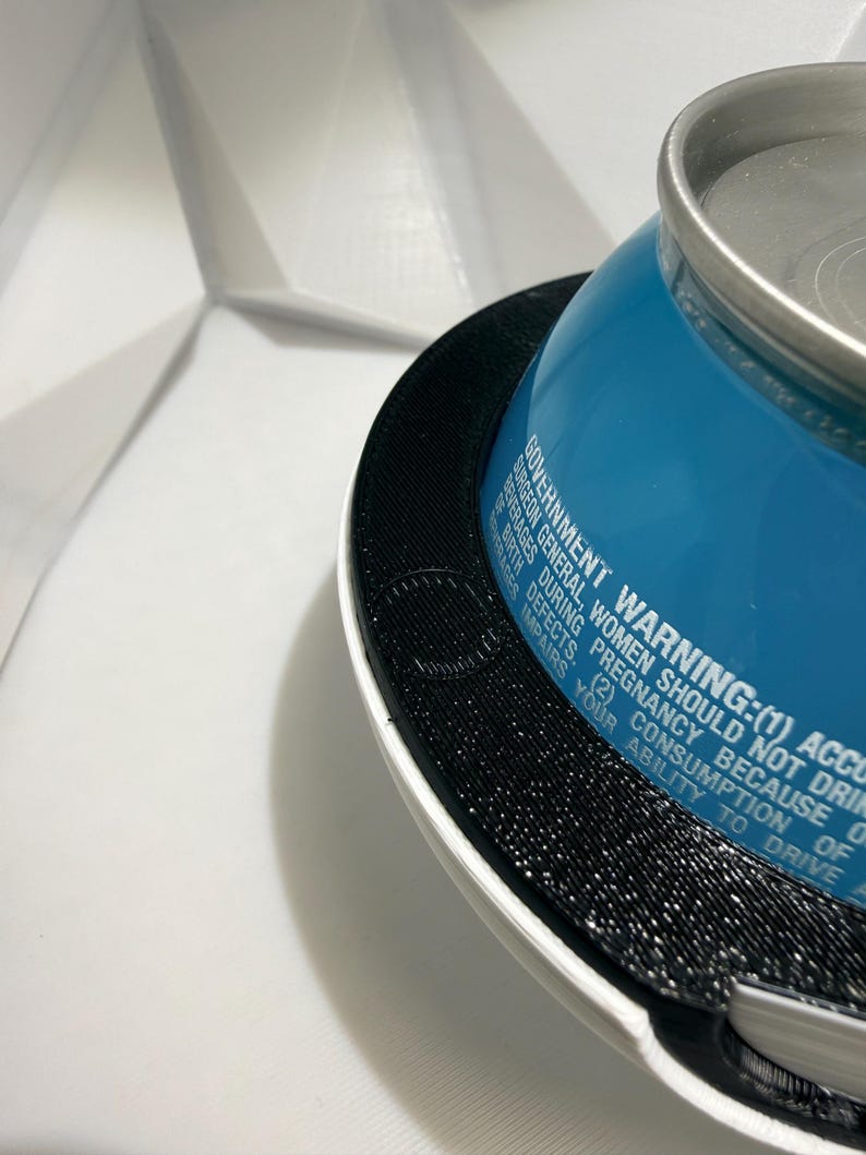 May include: A close-up shot of a blue beverage can with a silver top, resting on a black and white textured surface. The can has white text that reads, "GOVERNMENT WARNING: (1) ACCORDING TO THE SURGEON GENERAL, WOMEN SHOULD NOT DRINK..."