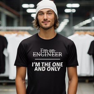 Könnte beinhalten: Ein Mann trägt eine weiße Mütze und ein schwarzes T-Shirt mit dem Aufdruck "I'm an ENGINEER I'M THE ONE AND ONLY".