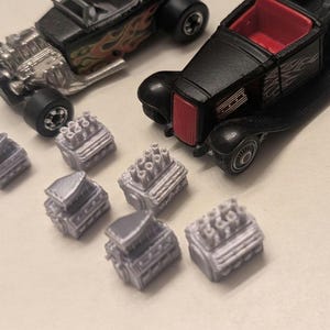 May include: A collection of toy cars and miniature engine models. Two black toy cars are visible, one with a red interior and the other with flame decals. Several small, silver-colored engine models are also present.