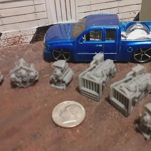 May include: A blue toy pickup truck with a silver bed is next to several gray miniature engine models. A dime is also present, providing a size reference for the small engine parts.