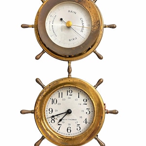 Könnte beinhalten: Zwei Wanduhren im nautischen Stil. Die obere Uhr ist ein Barometer mit weißem Zifferblatt und Messingrahmen. Die untere Uhr ist eine Seth Thomas Uhr mit weißem Zifferblatt und schwarzen Zeigern. Beide haben Rahmen im Schiffsrad-Stil.
