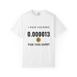 May include: White t-shirt with the text "I PAID FUCKING 0.0000013 FOR THIS SHIRT" in black font. A gold Bitcoin symbol is featured below the numbers. The shirt is a casual, crew neck style.