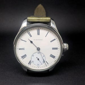 K&ouml;nnte beinhalten: Eine silberfarbene Armbanduhr mit wei&szlig;em Zifferblatt und schwarzen r&ouml;mischen Ziffern. Die Uhr hat ein kleines Sekunden-Zifferblatt und ein gr&uuml;nes Lederarmband. Auf dem Zifferblatt steht "SF. NETHERHOL".