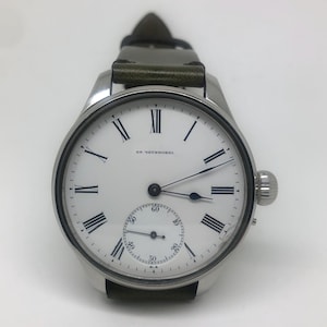 K&ouml;nnte beinhalten: Eine silberne Armbanduhr mit wei&szlig;em Zifferblatt, schwarzen r&ouml;mischen Ziffern und einem kleinen Sekundenzeiger. Die Uhr hat ein dunkelgr&uuml;nes Lederarmband und eine Aufzugskrone an der Seite.