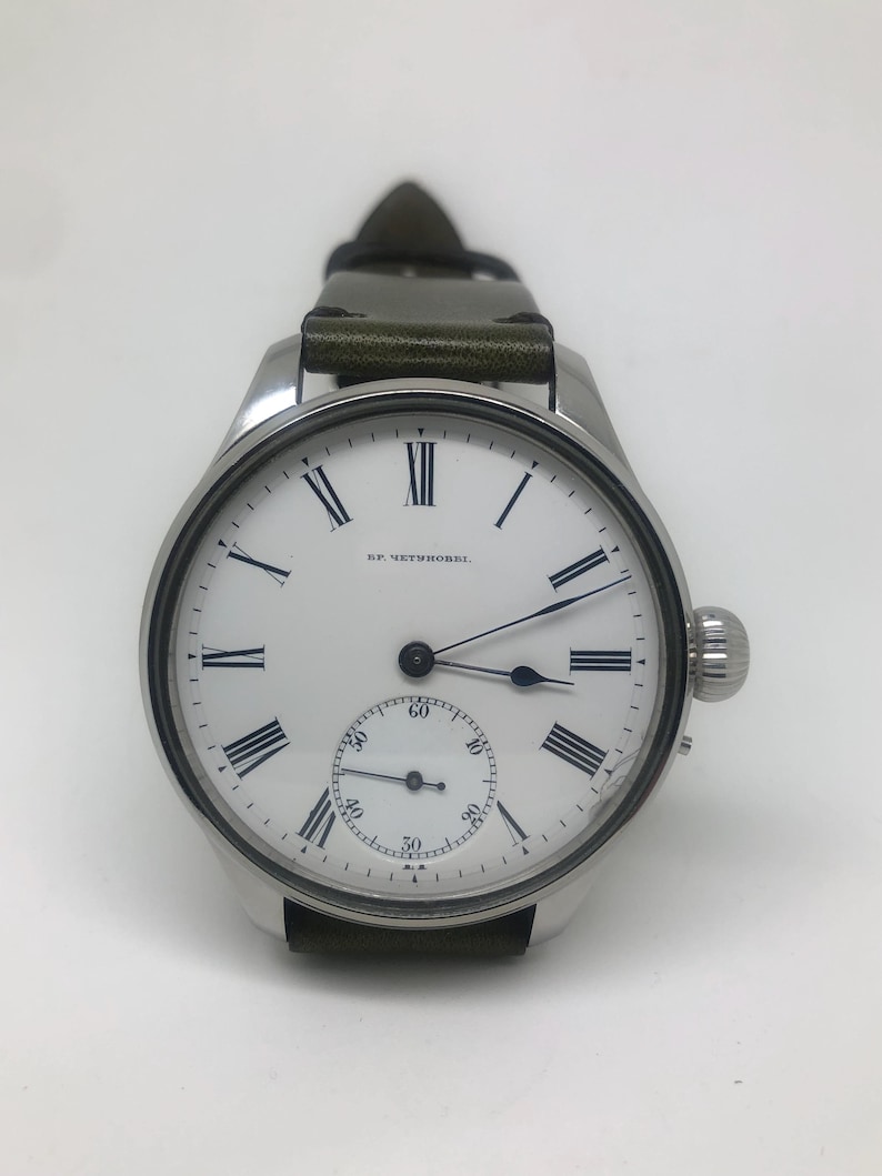 K&ouml;nnte beinhalten: Eine silberne Armbanduhr mit wei&szlig;em Zifferblatt, schwarzen r&ouml;mischen Ziffern und einem kleinen Sekundenzeiger. Die Uhr hat ein dunkelgr&uuml;nes Lederarmband und eine Aufzugskrone an der Seite.