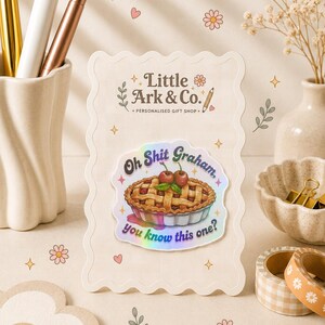 May include: A rectangular card with scalloped edges featuring the text Little Ark & Co. Personalised Gift Shop and a holographic sticker of a cherry pie. The sticker displays the text Oh Shit Graham, You know this one? with a pie illustration.