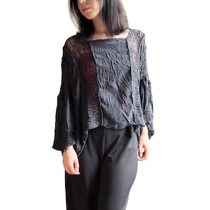Puede incluir: Un top negro de crochet de corte holgado y mangas largas. El top tiene un diseño en capas con una superposición de crochet transparente y una capa inferior negra lisa.
