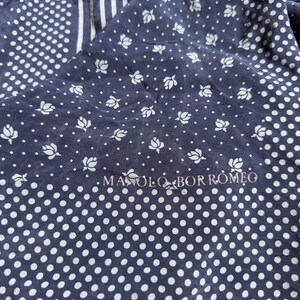Puede incluir: Una tela de patrón azul y blanco con el texto "MANOLO BORROMEO" impreso en blanco. La tela tiene un patrón de lunares y un patrón floral.