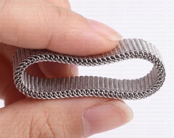 May include: A silver-toned metal mesh band with a flexible, woven link structure. The band is formed into an oval loop shape, showcasing a consistent, fine-textured pattern throughout its surface. The text NOCTELLE JEWELRY appears in the top corner.