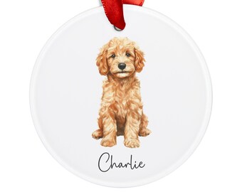 May include: A round white ceramic ornament with a watercolor illustration of a light brown puppy sitting. The puppy has a white chest and a black nose. The ornament has the name "Charlie" written in black cursive.