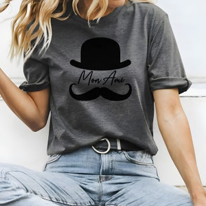 May include: A gray t-shirt with a black bowler hat, mustache, and the text "Mon Ami" printed on the front.