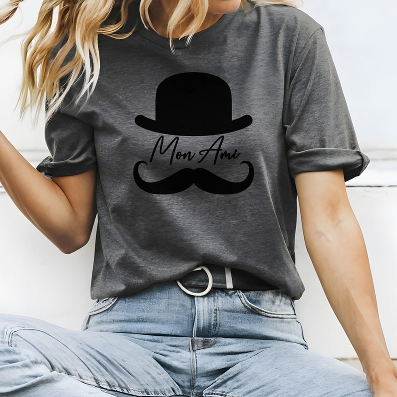 May include: A gray t-shirt with a black bowler hat, mustache, and the text "Mon Ami" printed on the front.