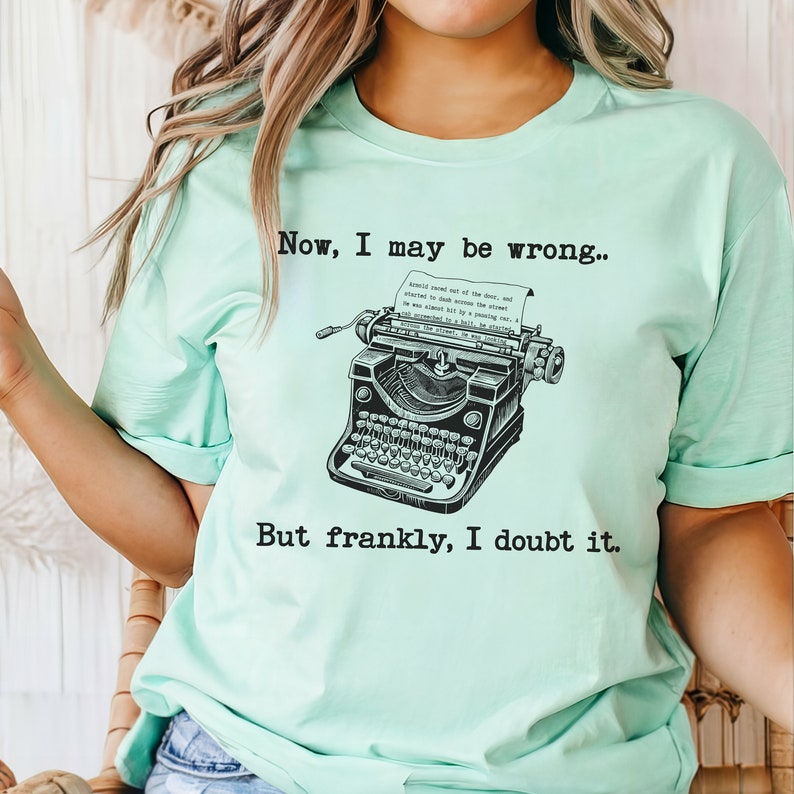 May include: A light blue t-shirt with a black and white illustration of a vintage typewriter. The text on the shirt reads "Now, I may be wrong... But frankly, I doubt it."