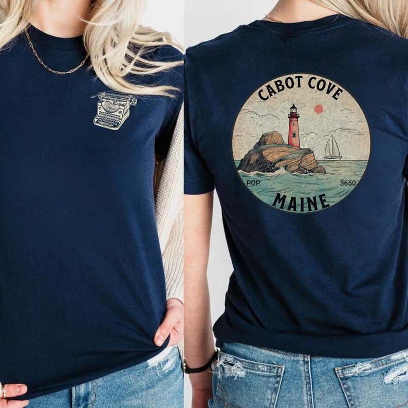 Puede incluir: Una camiseta azul marino con una ilustraci&oacute;n vintage de un faro en la parte posterior. La ilustraci&oacute;n est&aacute; en un c&iacute;rculo con el texto "CABOT COVE MAINE POP 3650".