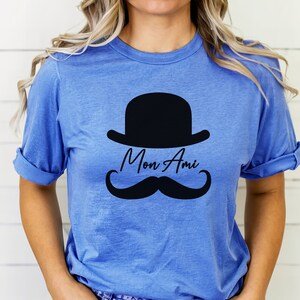 May include: A blue t-shirt with a black bowler hat, mustache, and the text "Mon Ami" printed on the front.