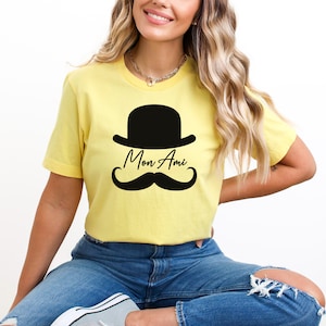 May include: A yellow t-shirt with a black bowler hat, mustache, and the text "Mon Ami" printed on the front.