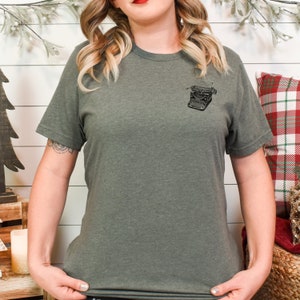 Puede incluir: Una camiseta verde oscuro con un gr&aacute;fico de m&aacute;quina de escribir vintage en el pecho izquierdo. La m&aacute;quina de escribir es en blanco y negro.