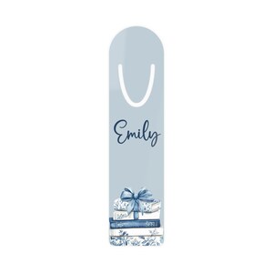 May include: A pale blue bookmark with a white curved top and the name "Emily" in navy script. The bottom of the bookmark features a stack of books with a blue bow and floral detailing.