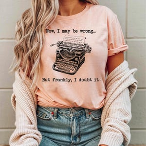 May include: A pink t-shirt with a vintage typewriter graphic and the text "Now, I may be wrong... But frankly, I doubt it."
