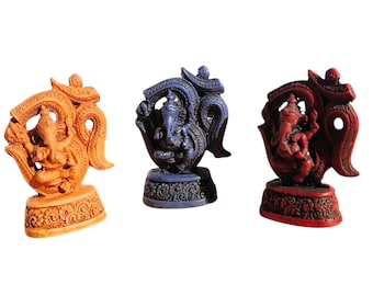 May include: Three small statues of the Hindu deity Ganesha, each with a different coloured base. The statues are made of a dark brown material and are painted in shades of orange, blue, and red. The statues are all in the same pose, with Ganesha sitting on a lotus flower and holding a sweet in his trunk.
