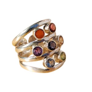 May include: Silver ring with seven colorful gemstones set in a multi-band design.