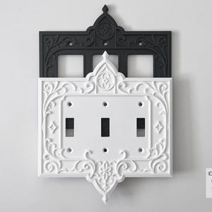 May include: Ornate white and black light switch cover with three switch openings. The white section has a decorative floral design. The black section above has a matching design. The text "Darkka Studio. Original design. Any other listing is an infringement." is in the bottom right corner.