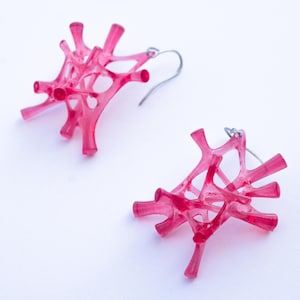 May include: A pair of pink resin earrings with a delicate, intricate design. The earrings are lightweight and have a modern, geometric look.