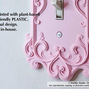 Puede incluir: Una placa de interruptor de luz rosa impresa en 3D con un dise&ntilde;o ornamental y arremolinado. La cubierta est&aacute; hecha de pl&aacute;stico de origen vegetal y presenta un interruptor basculante est&aacute;ndar. El texto en la cubierta dice "3D printed with plant-based eco-friendly PLASTIC."