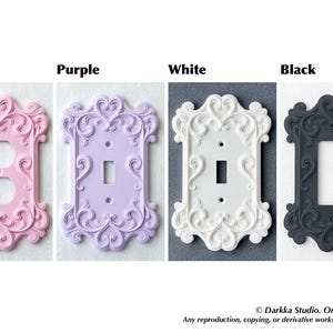 Puede incluir: Cuatro cubiertas decorativas para interruptores de luz en rosa, morado, blanco y negro. Cada cubierta tiene un dise&ntilde;o ornamental y con volutas. La cubierta rosa tiene dos agujeros para un enchufe, mientras que las otras tienen una abertura para un solo interruptor.