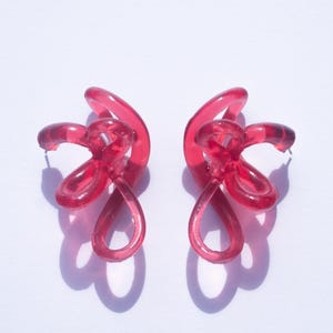 May include: A pair of pink resin earrings with a unique, twisted design. The earrings are lightweight and have a modern, abstract look.