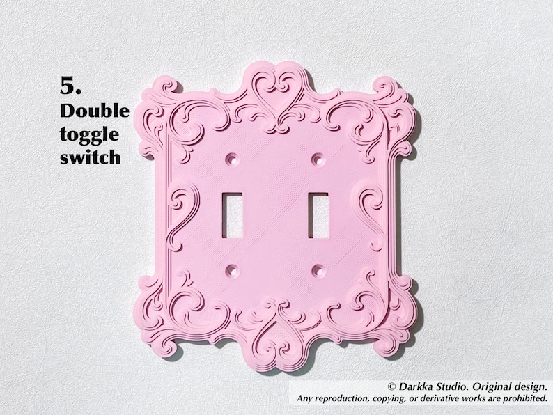 Puede incluir: Una placa de interruptor doble basculante rosa con un dise&ntilde;o ornamental de volutas. El texto "5. Double toggle switch" es visible. El dise&ntilde;o incluye dos aberturas para interruptores y orificios para tornillos. Es un elemento decorativo para el hogar.