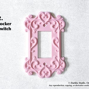 Puede incluir: Una cubierta rosa para interruptor basculante con un dise&ntilde;o ornamental de volutas. La cubierta tiene una abertura rectangular para el interruptor y est&aacute; etiquetada como "2. rocker switch".