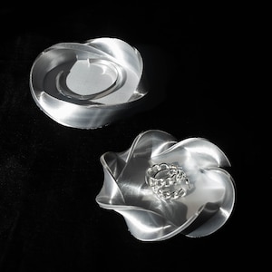 May include: Two silver metal ring dishes, one with a silver ring inside. The dishes are shaped like a flower with multiple petals.