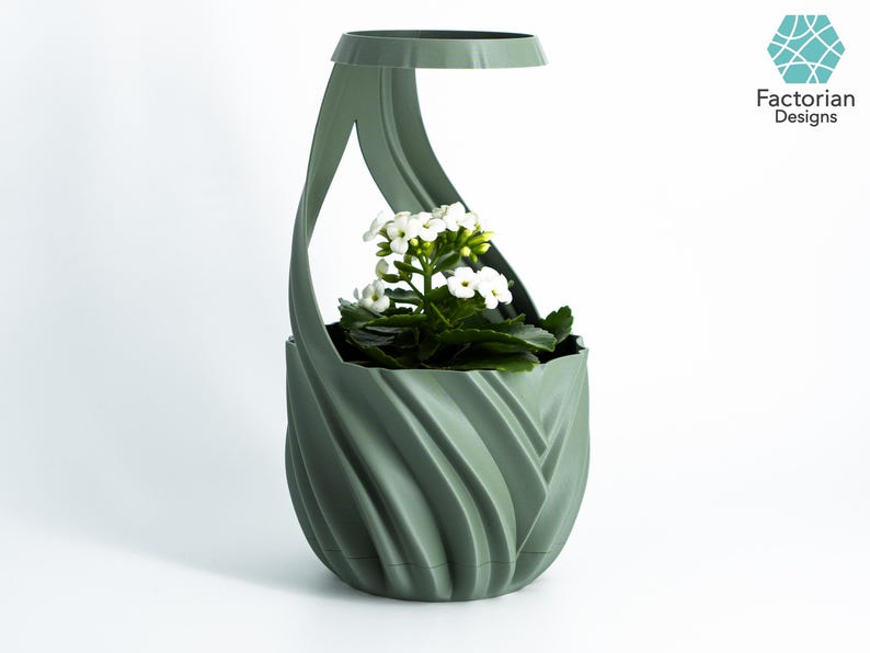 K&ouml;nnte beinhalten: Ein salbeigr&uuml;ner, 3D-gedruckter Pflanztopf mit einem einzigartigen, wirbelnden Design. Der Pflanztopf enth&auml;lt eine kleine wei&szlig; bl&uuml;hende Pflanze mit gr&uuml;nen Bl&auml;ttern. Der Pflanztopf hat einen Griff und den Text "Factorian Designs".