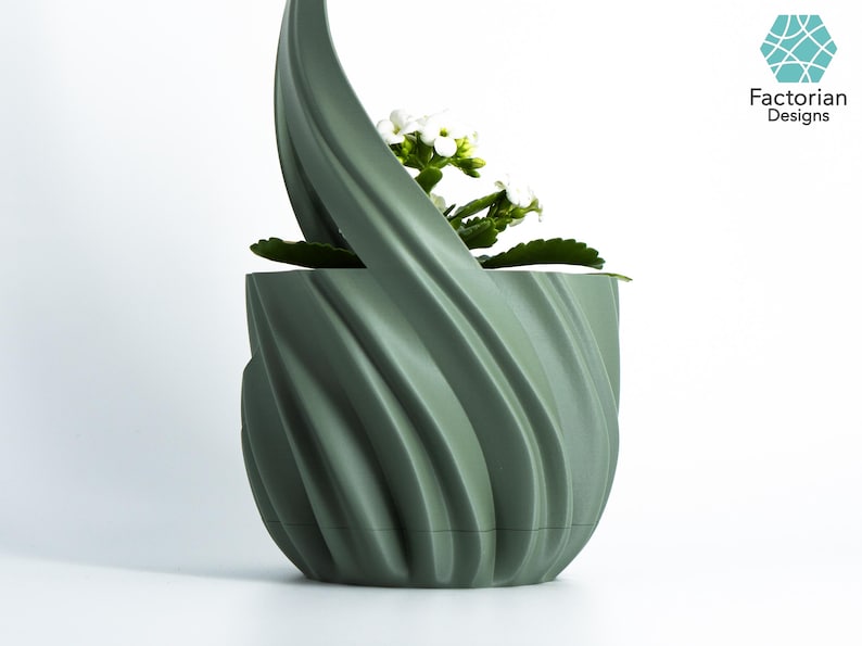 K&ouml;nnte beinhalten: Ein salbeigr&uuml;ner, 3D-gedruckter Pflanzentopf mit einem einzigartigen, wirbelnden Design. Der Topf enth&auml;lt eine kleine Pflanze mit wei&szlig;en Bl&uuml;ten und gr&uuml;nen Bl&auml;ttern. Das Logo von Factorian Designs ist sichtbar.