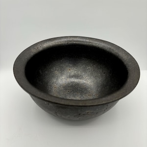 以下が含まれることがあります： わずかに広がった縁を持つ黒いセラミックボウル。ボウルはテクスチャ加工された表面とわずかに不均一な底を持っています。