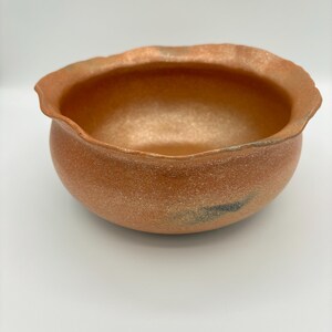 以下が含まれることがあります： 波打つ縁のあるテラコッタ色のセラミックボウル。ボウルは斑点模様の質感で、薄い青色の釉薬がかかっています。