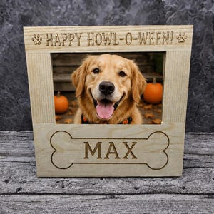 May include: A light-colored wooden picture frame featuring the engraved text HAPPY HOWL-O-WEEN! at the top with paw prints on each side. The frame displays a photo of a golden retriever and has a bone-shaped cutout at the bottom with the name MAX.